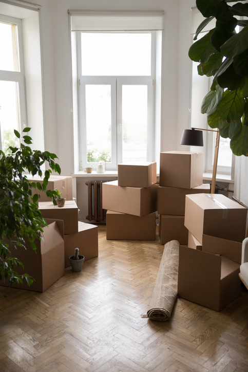 Stacks of cardboard boxes packed for moving, placed on floor at window in apartment. 