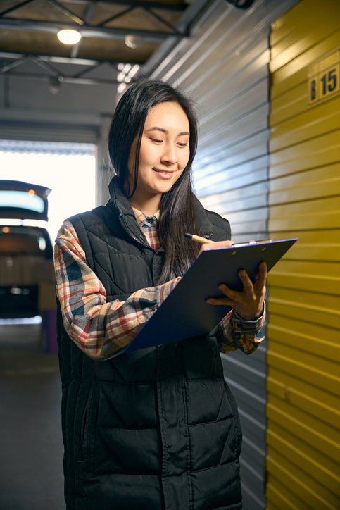 Woman writing in a folder while standing in a storage unit