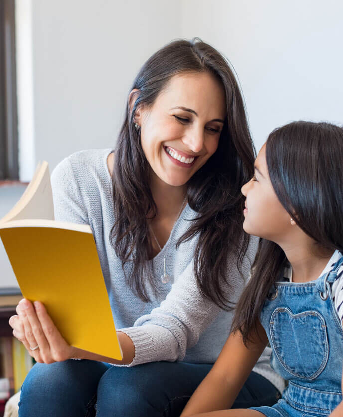 Happy woman reading story book to little girl. 