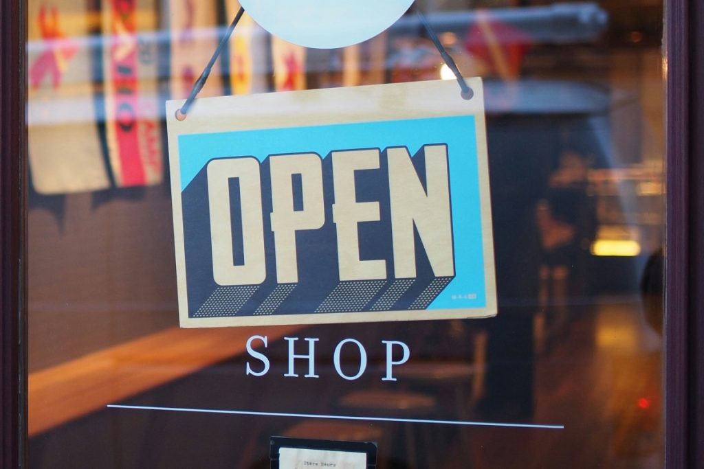 A sign that says Open hangs in a window above the word Shop etched into the glass. Behind the glass door you can see a counter with artwork hanging above it.