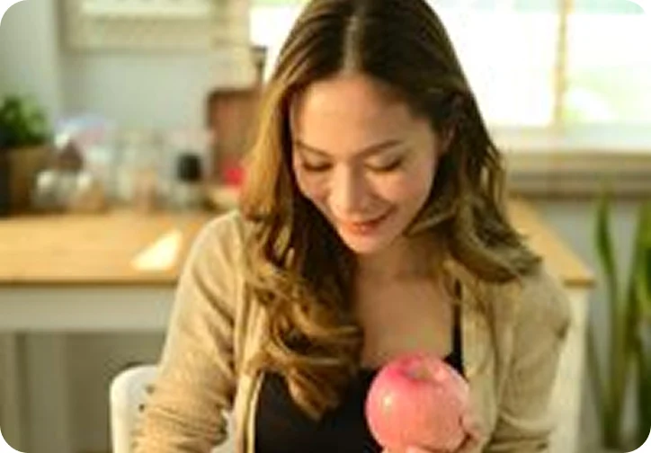 Woman holding an apple while looking down at a table in a sunlit kitchen